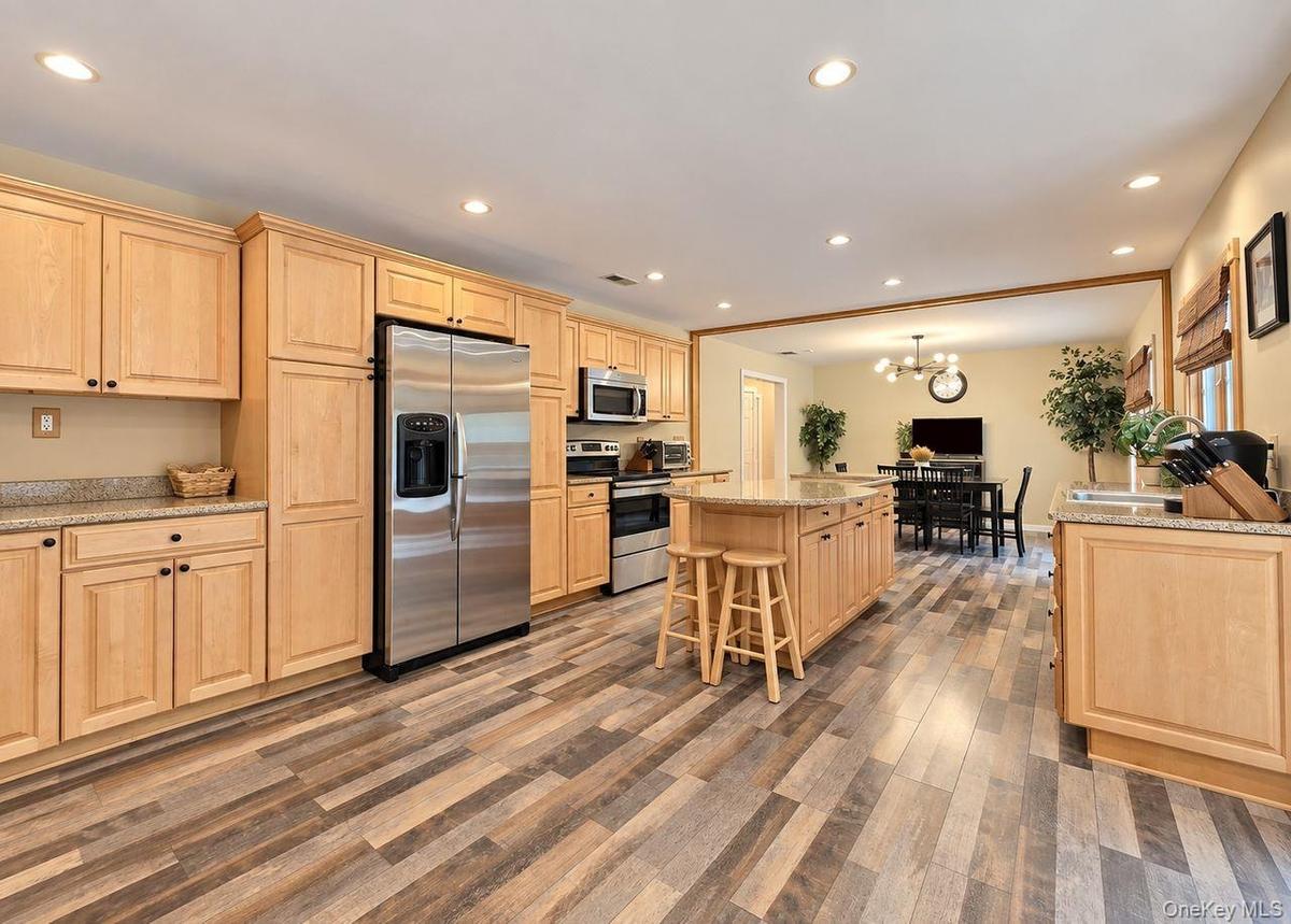 Spacious kitchen featuring wood-finish flooring, light wood cabinetry, stainless steel appliances, and an island with a stone countertop