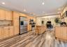 Spacious kitchen featuring wood-finish flooring, light wood cabinetry, stainless steel appliances, and an island with a stone countertop