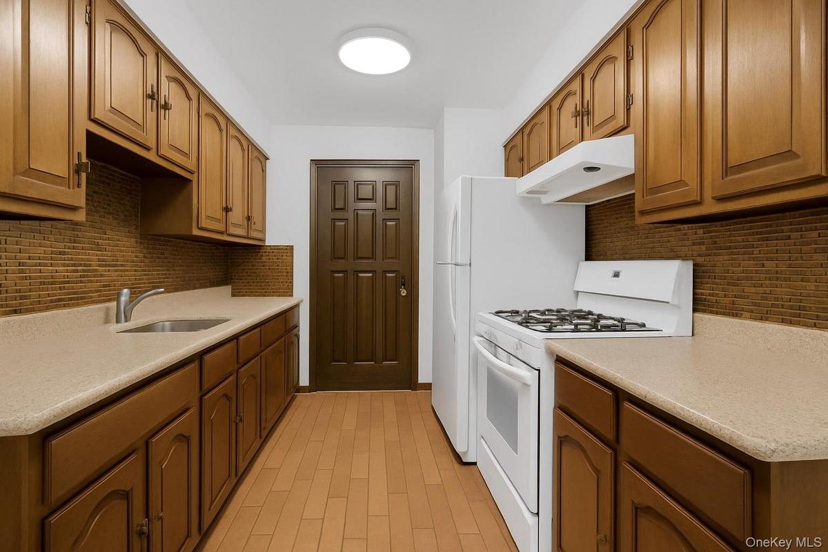 Kitchen with tasteful backsplash, white gas range, under cabinet range hood, and brown cabinets