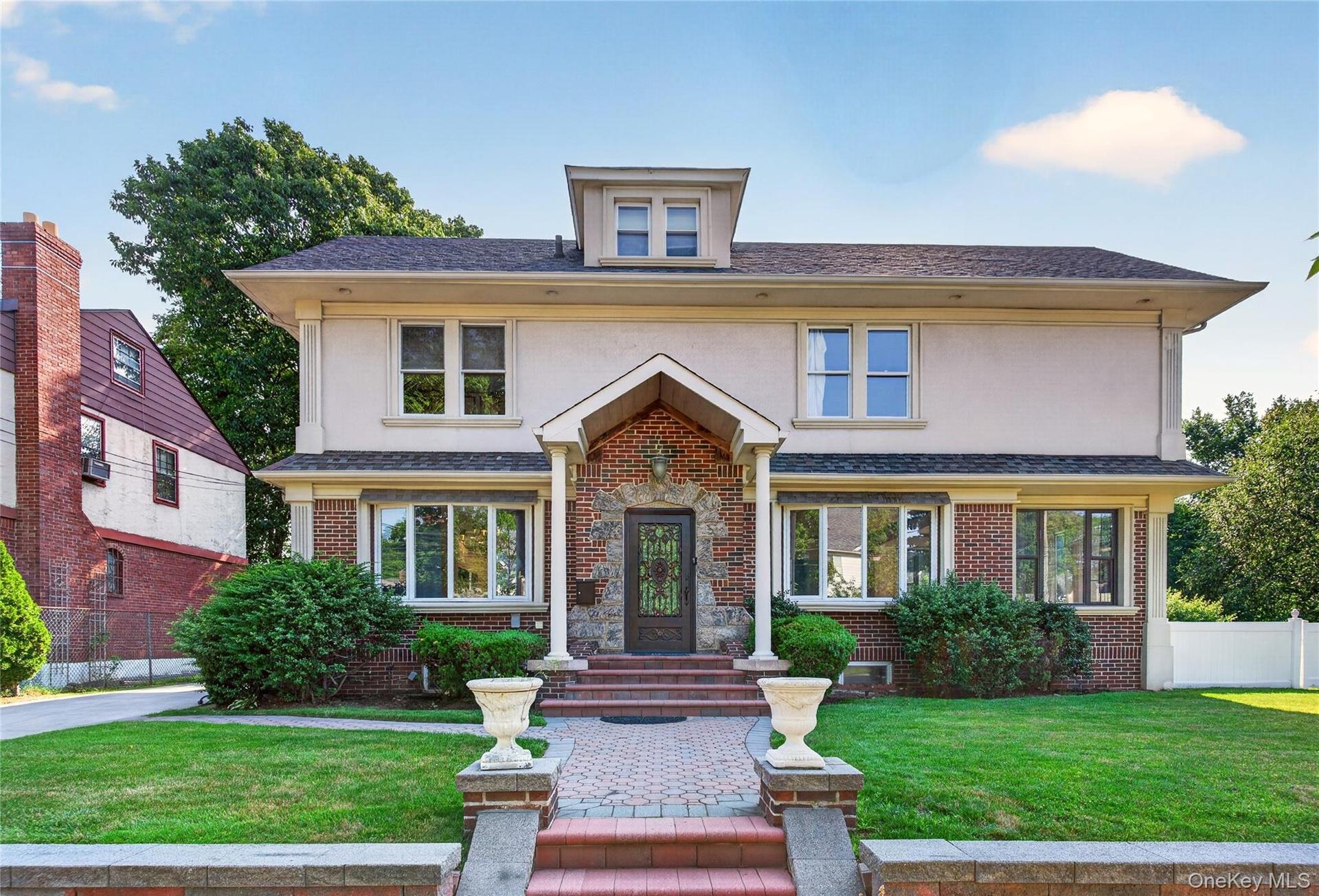 Traditional-style home featuring a brick and stucco facade, a prominent front entrance with stone accents, a dormer window, mature landscaping, and a 
