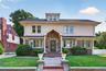 Traditional-style home featuring a brick and stucco facade, a prominent front entrance with stone accents, a dormer window, mature landscaping, and a 