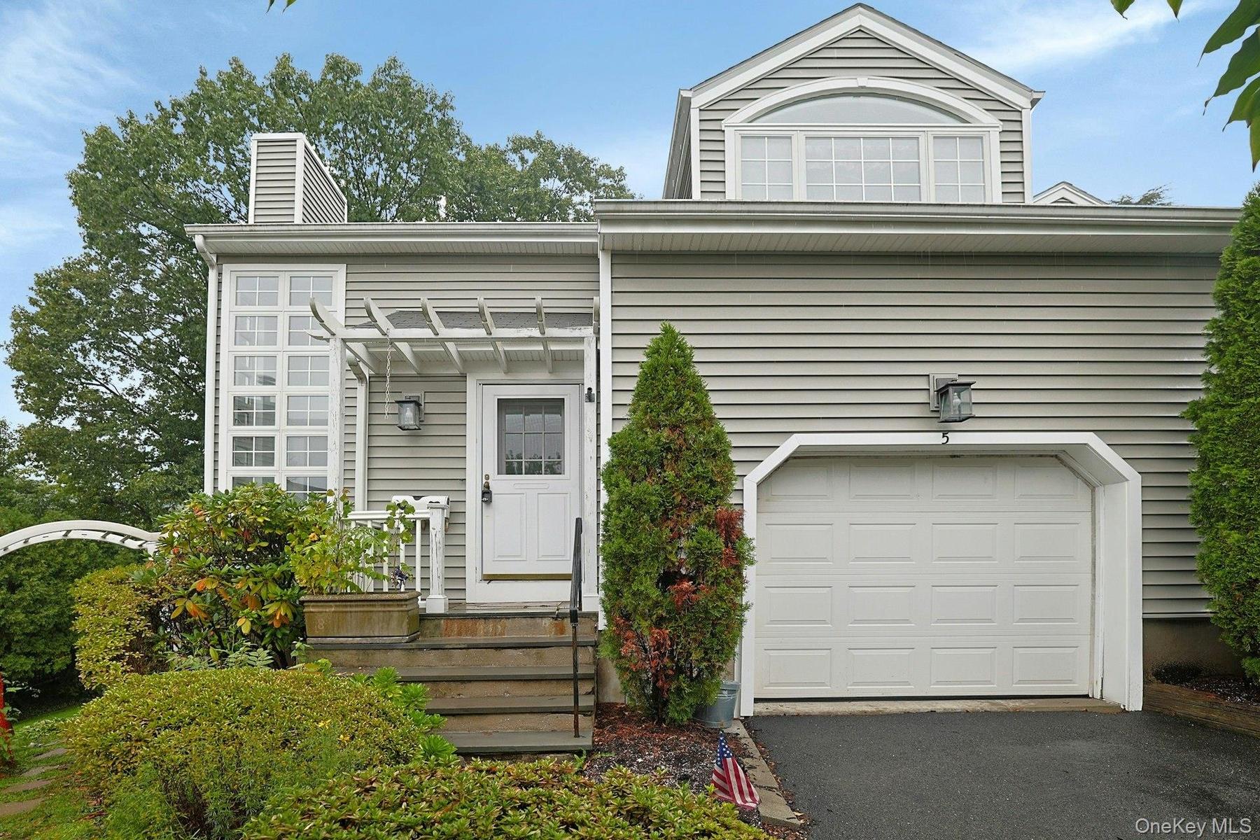 Siding exterior with a paneled garage door, arched window, and a white front entry door with an overhead pergola