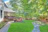 Expansive backyard featuring a manicured lawn, established trees, and a covered porch with a wood railing