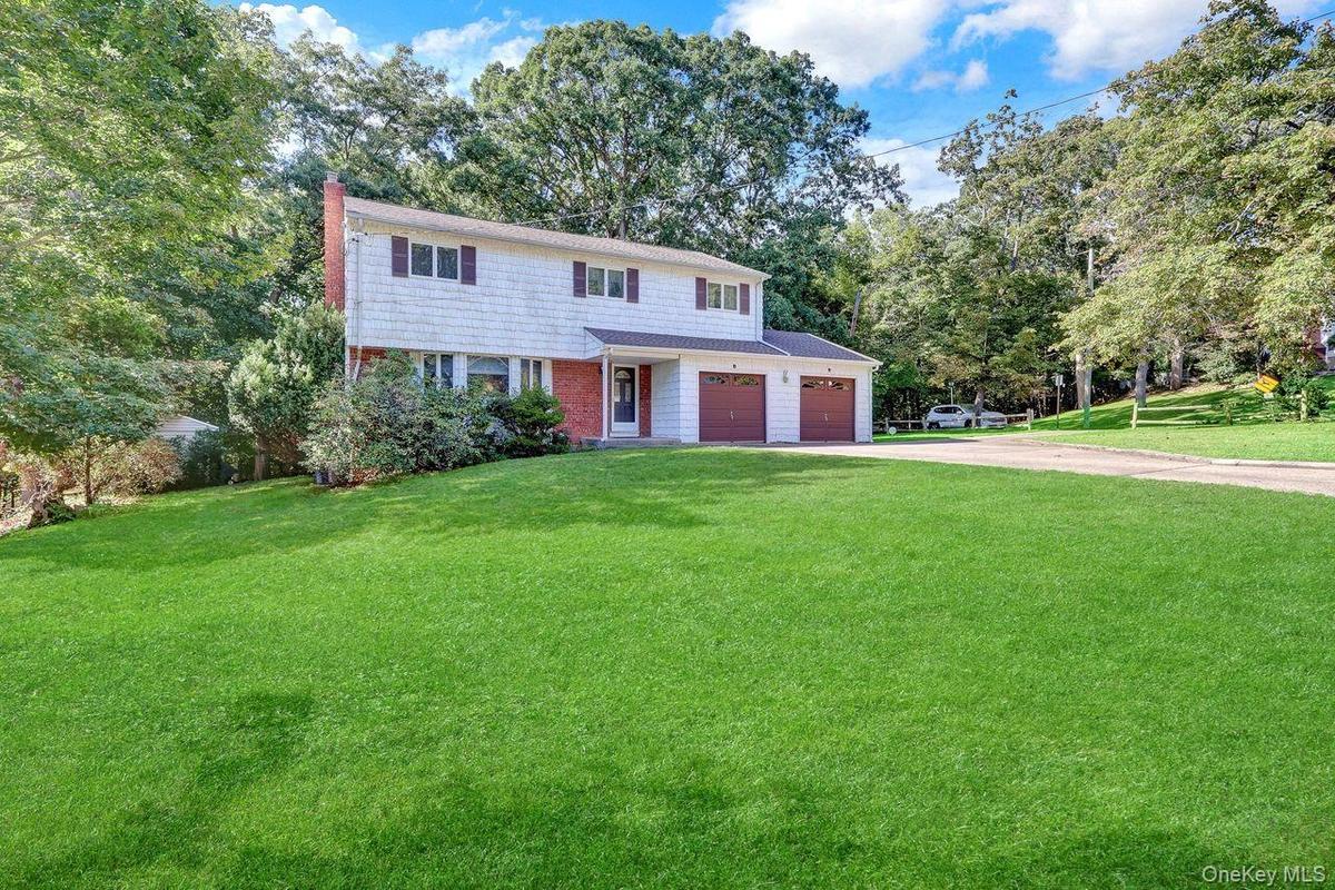 Two-story Colonial with white shake siding and brick accents, featuring a two-car garage duel driveway, on a corner lot.