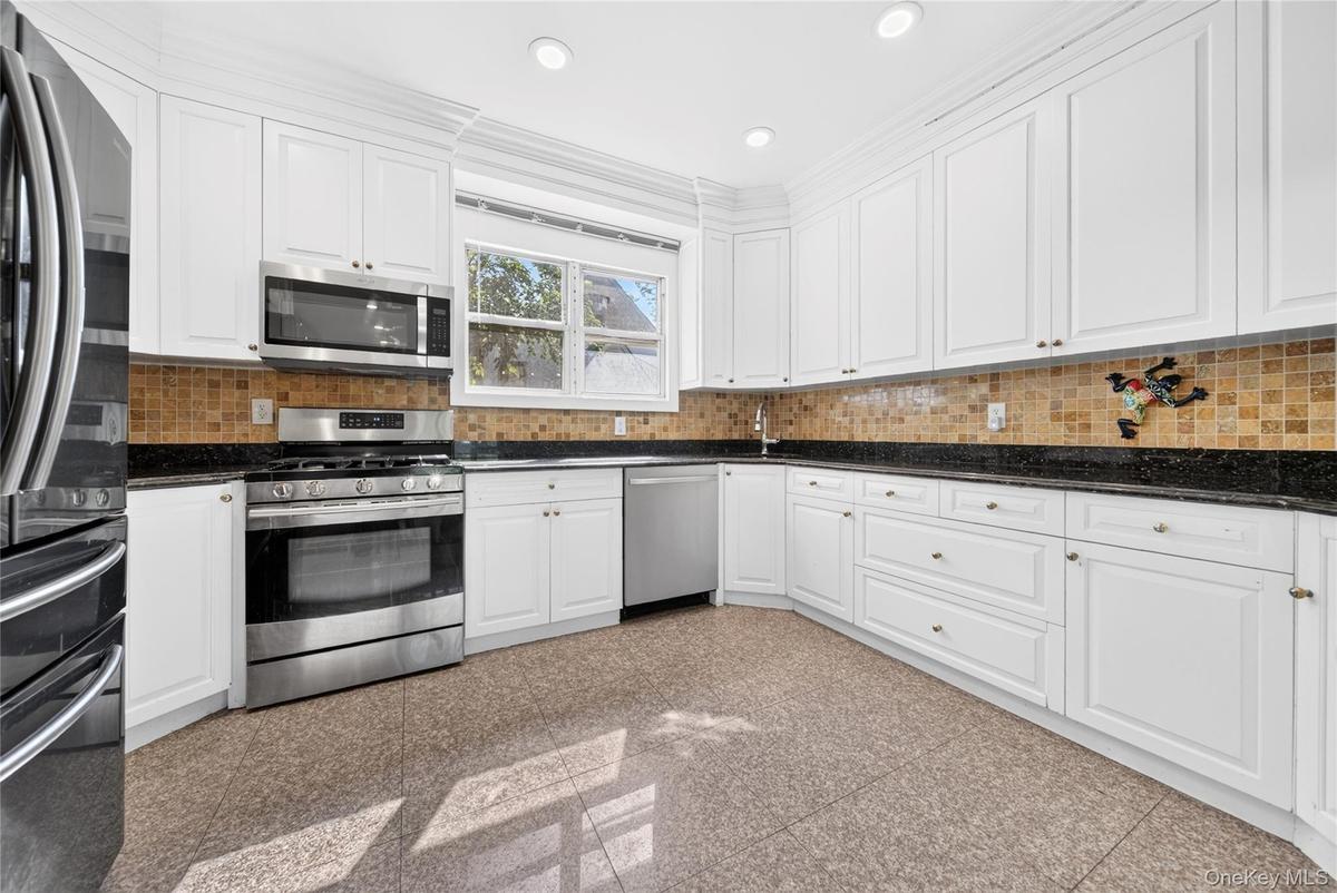 Kitchen featuring extensive white cabinetry, stainless steel appliances, dark countertops, a tiled backsplash, and recessed lighting