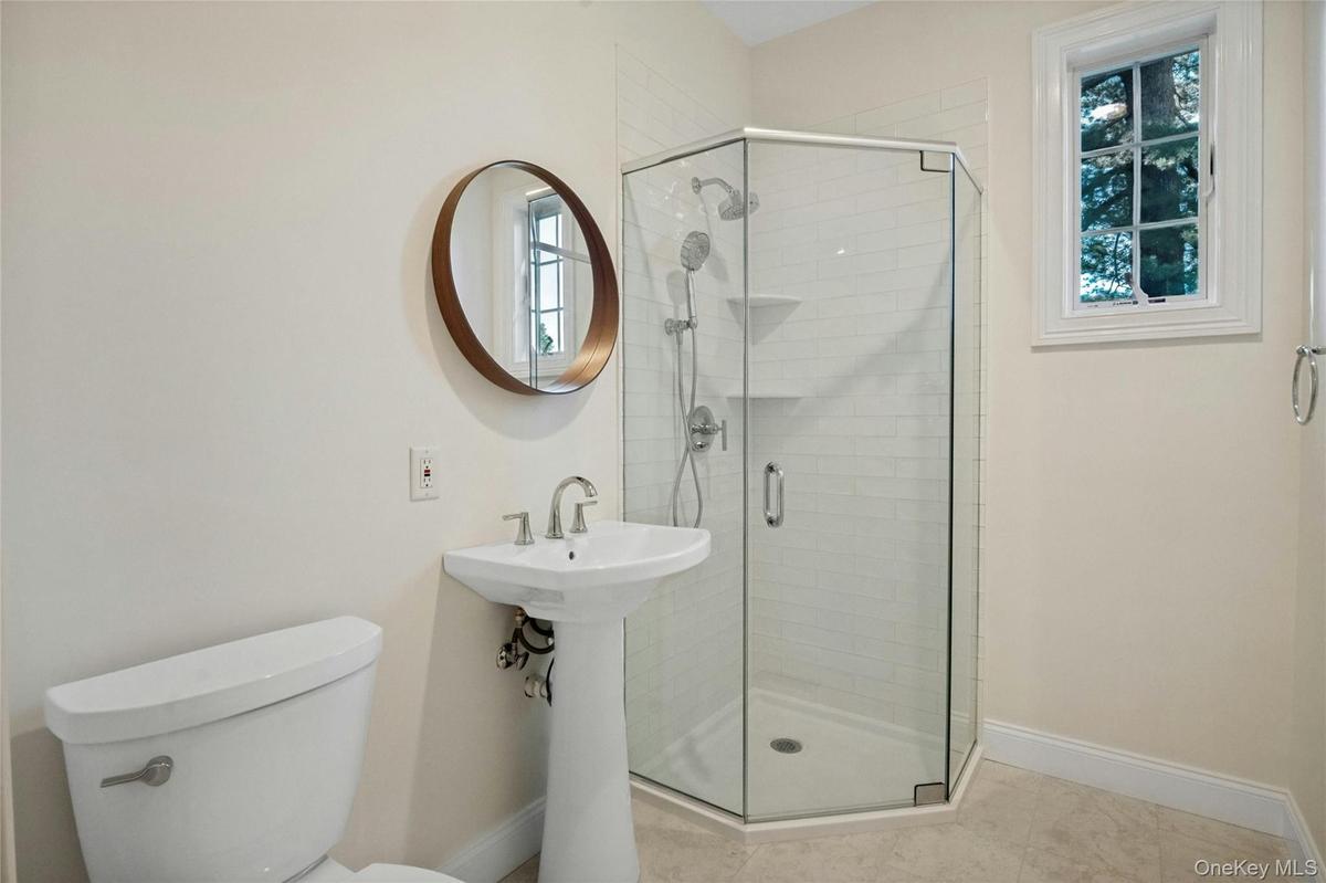 First floor hall bathroom with pedestal sink with polished chrome fixtures, frameless glass shower enclosure with subway tile surround, window with wh