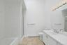 The primary bathroom, with tiled floor and a high ceiling that rises up to a skylight, is a private oasis. The long vanity is very usable, and there i