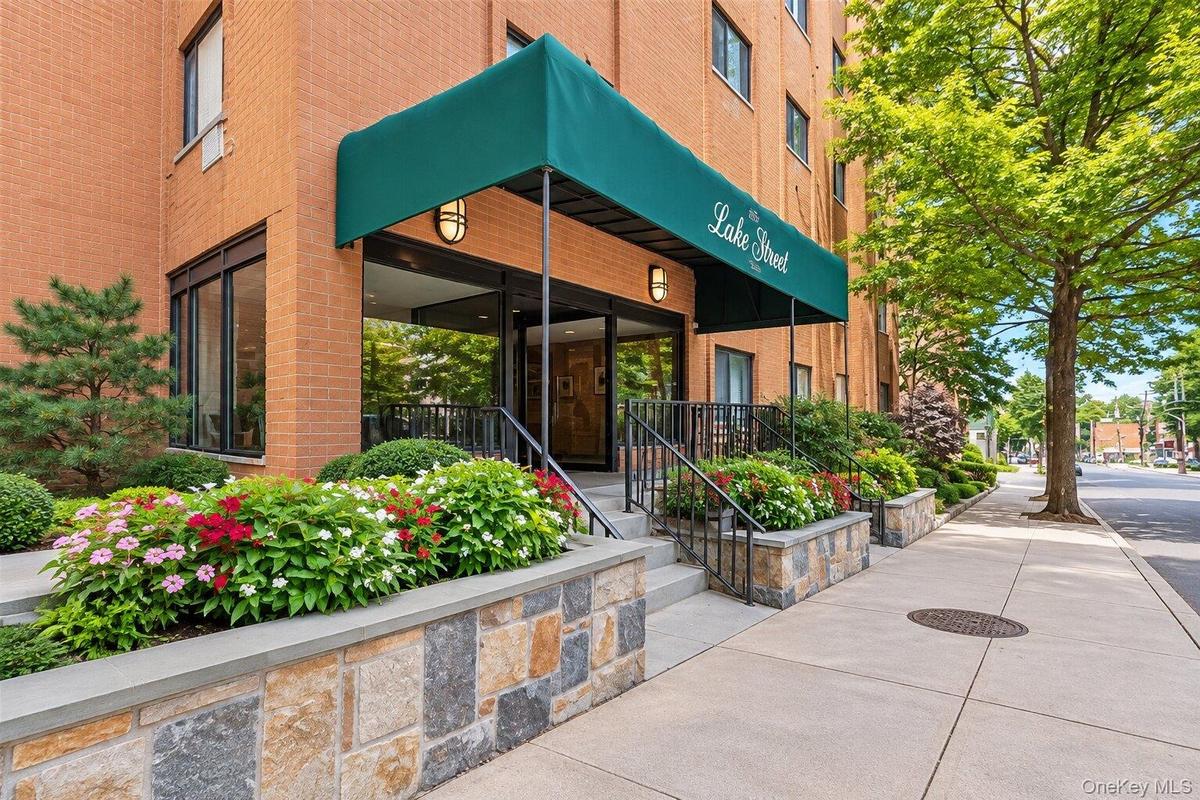 Brick facade building featuring a green awning, stone-clad planters, wrought iron railings, and extensive landscaping