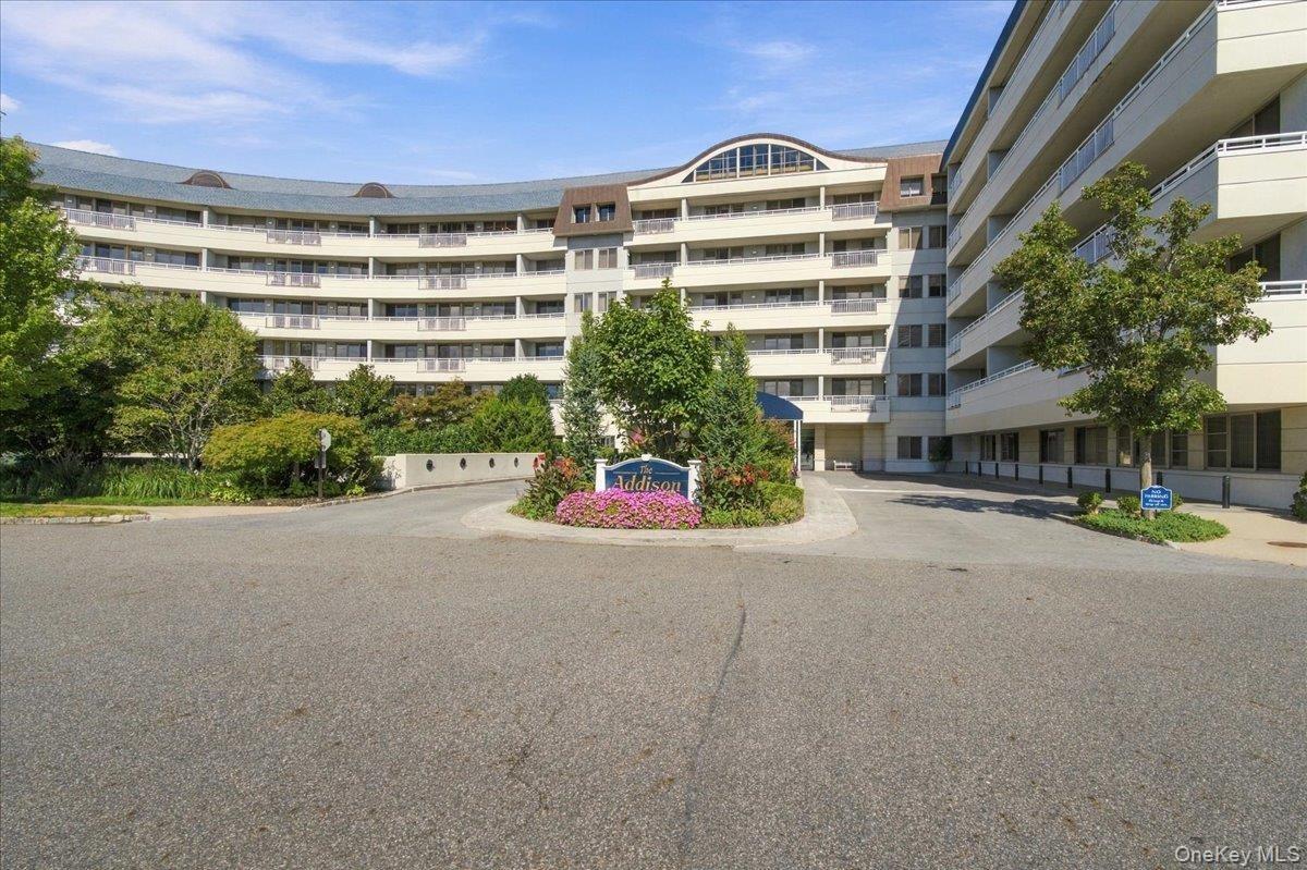 Curved facade with multiple levels of private balconies, accented by a prominent entrance and lush landscaping