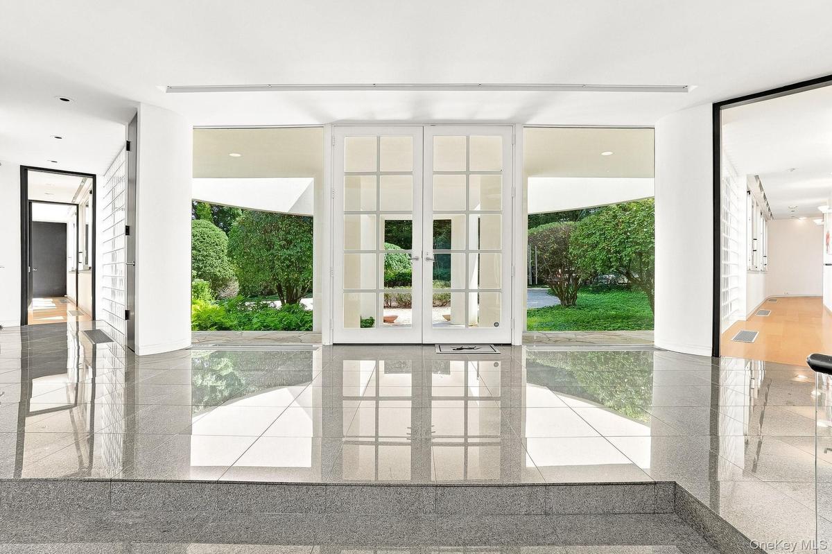 Polished granite-style tile floors and expansive floor-to-ceiling windows flood this striking modern foyer with lush green views.