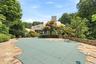 An expansive stone patio surrounds a private, tree-lined swimming pool overlooked by the striking modern estate facade.