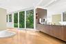 A spa-like master bathroom featuring a wood vanity, an inset jetted tub, and sliding glass doors with serene nature views.