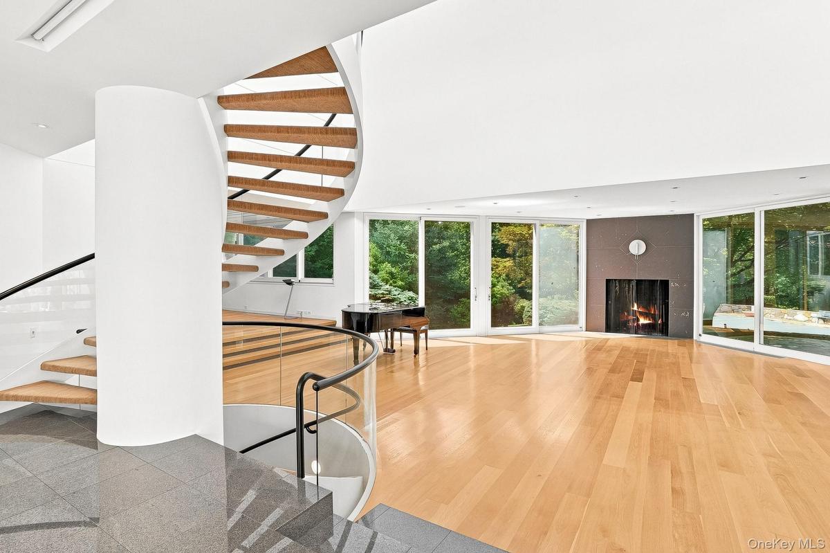 Striking architectural design defines the main living area, featuring an elegant curved staircase, a cozy fireplace, and space for a grand piano.