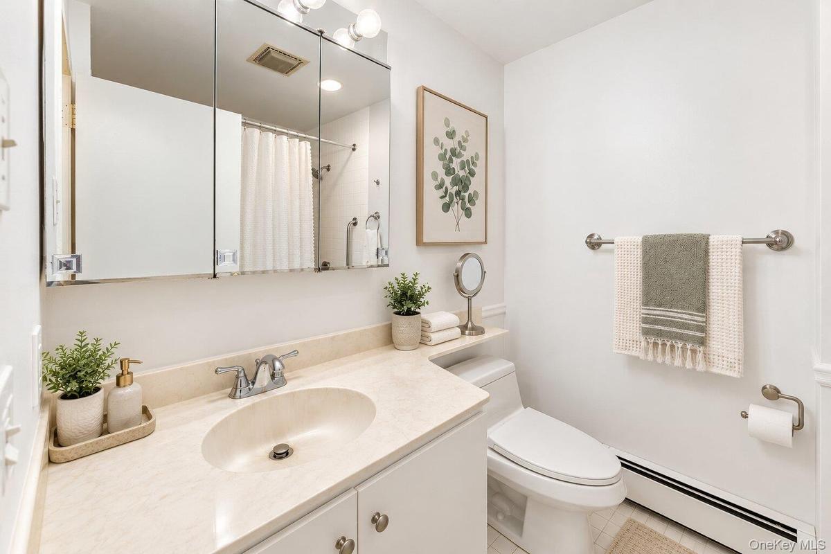Vanity with an integrated sink and light-colored countertop, wall-mounted medicine cabinet with mirror, and a toilet with an adjacent shelf