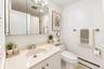 Vanity with an integrated sink and light-colored countertop, wall-mounted medicine cabinet with mirror, and a toilet with an adjacent shelf