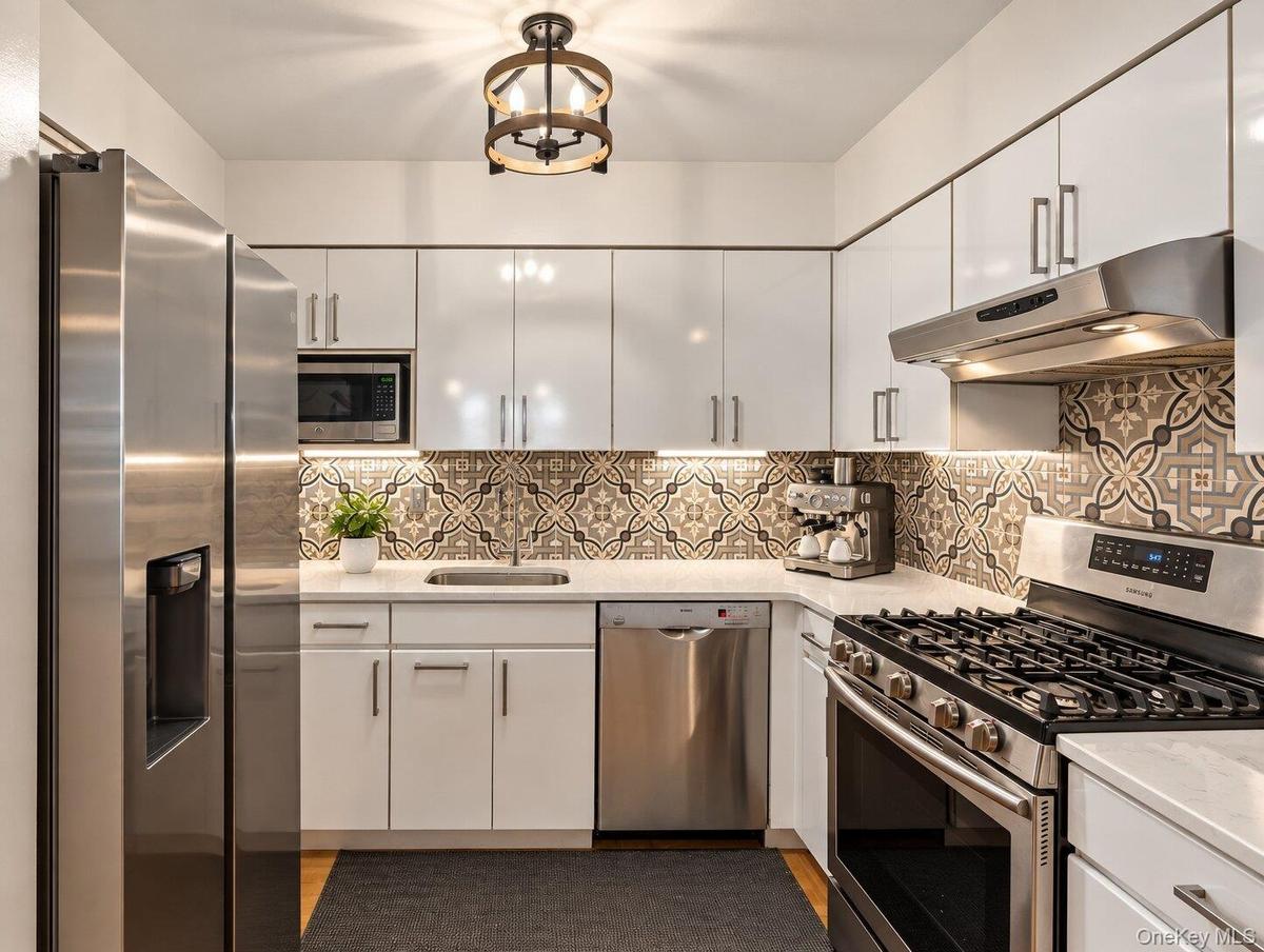 Contemporary kitchen featuring stainless steel appliances, white cabinetry, patterned tile backsplash, and light countertops