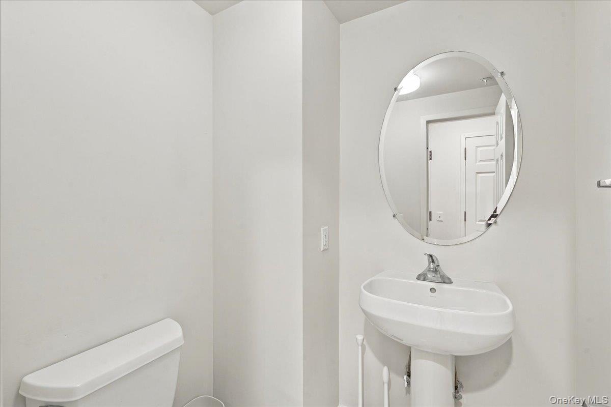 Pedestal sink, wall-mounted oval mirror, and white toilet