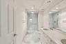 Double vanity with integrated sinks, frameless mirrored wall, glass-enclosed shower, tiled shower walls, and recessed lighting