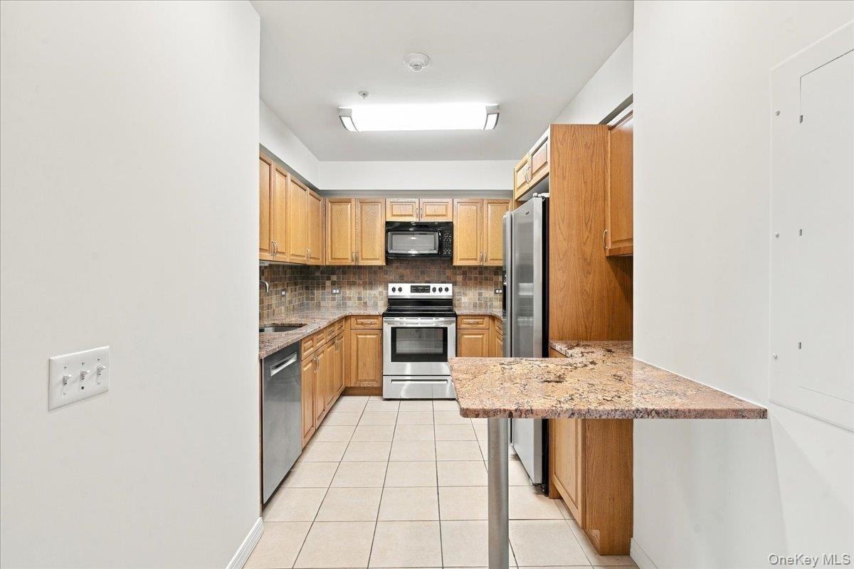 Kitchen featuring wood cabinetry, stainless steel appliances, a tiled backsplash, and a breakfast bar with a stone-finish countertop
