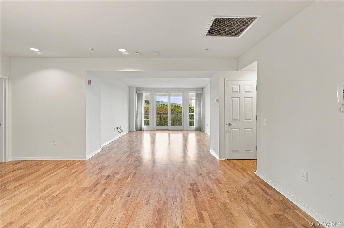 Wood-finish flooring throughout, recessed ceiling lighting, light-colored walls, and a large sliding glass door opening to an exterior balcony