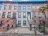 Stone facade with prominent cornice details, wrought iron fencing, and a classic stoop entrance