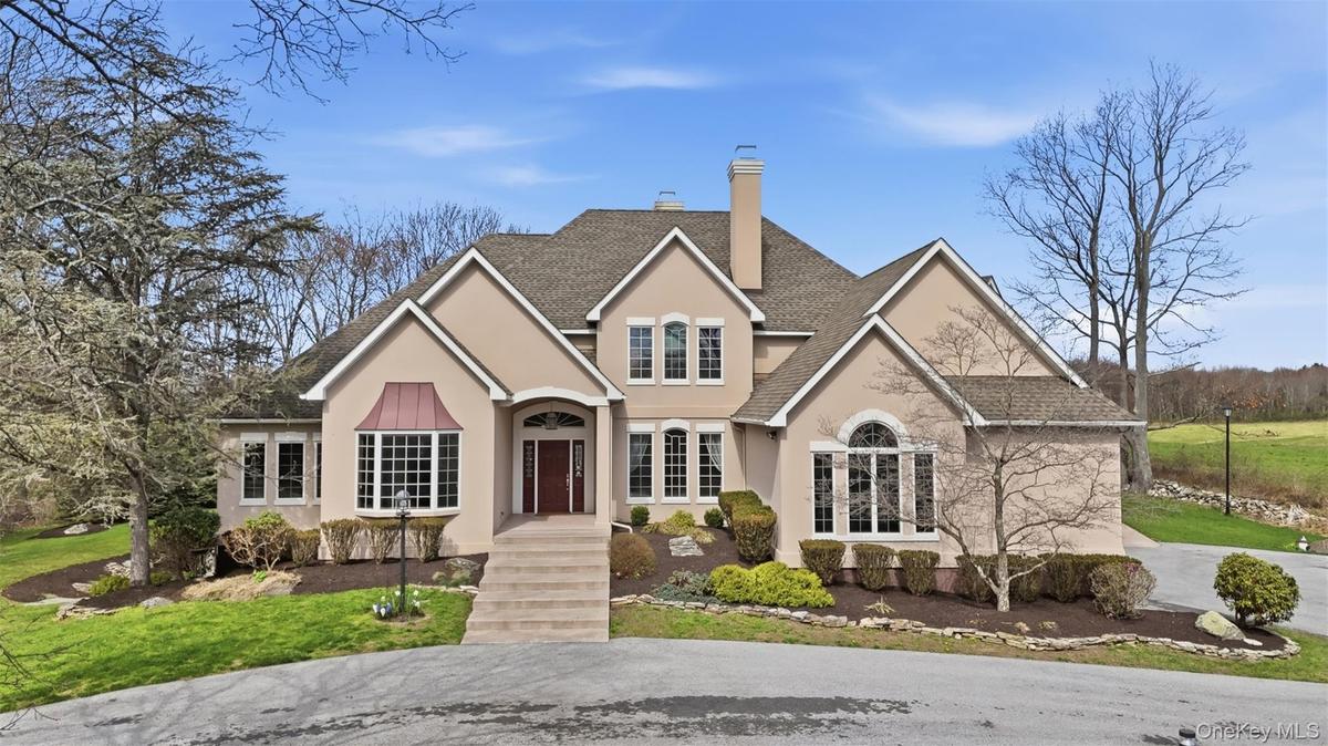 The property features a stucco exterior, a prominent front entrance with a dark red door and steps, and a bay window with a distinctive copper-colored