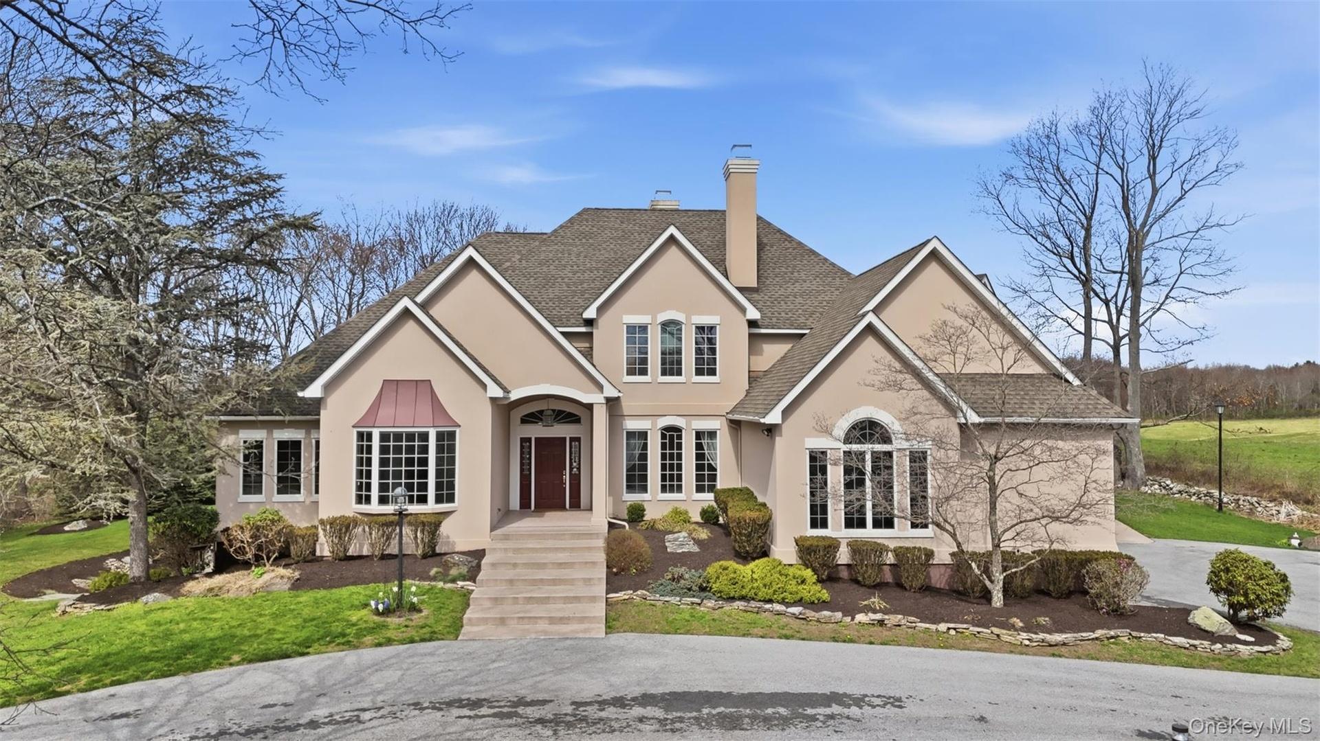The property features a stucco exterior, a prominent front entrance with a dark red door and steps, and a bay window with a distinctive copper-colored