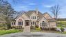 The property features a stucco exterior, a prominent front entrance with a dark red door and steps, and a bay window with a distinctive copper-colored