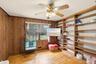 Wood-finish flooring, wood paneling, built-in shelving, ceiling fan with light fixture, and window with natural light