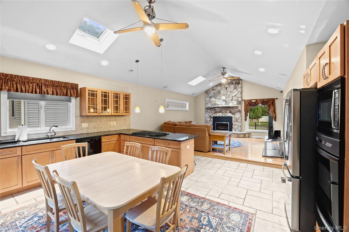 Kitchen featuring light wood cabinetry, black countertops, tile flooring, and a skylight