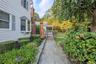 Shingle siding exterior with a bay window, brick chimney, stone paver walkway, and mature landscaping