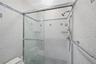 Glass-enclosed shower with a handheld shower fixture, overhead showerhead, and mosaic tile walls