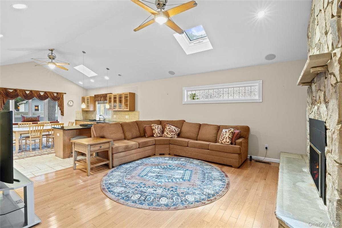 Vaulted ceilings, skylights, wood-finish flooring, a stone-clad fireplace with a hearth, and recessed lighting