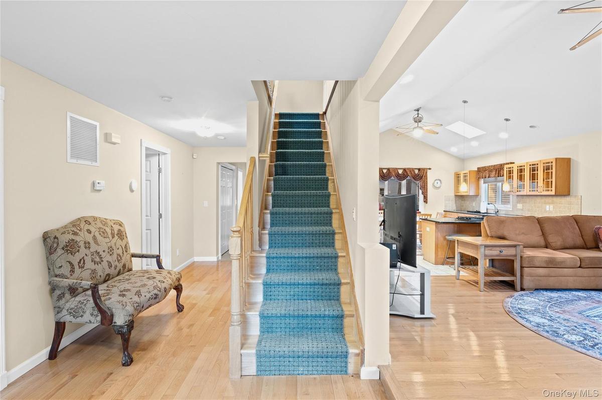 Hardwood-finish flooring, staircase with carpeting, open-concept design, vaulted ceiling, and skylight