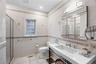 White ceramic tile flooring and wall accents, glass-enclosed shower, integrated sink vanity, multi-panel mirrored medicine cabinet, and a privacy wind