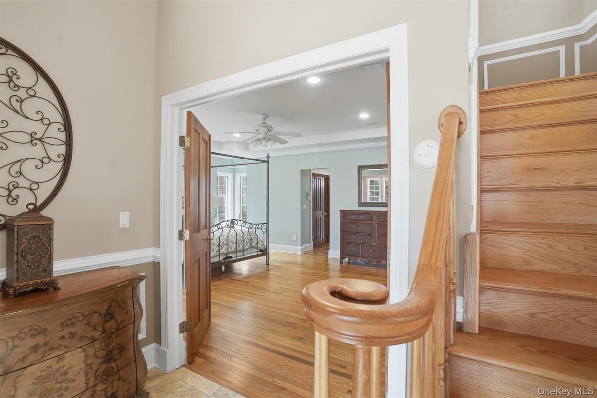 Entryway featuring a wooden staircase with a banister, wood flooring, and a doorway leading into a room with wood flooring and a ceiling fan
