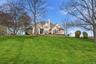 The property features a spacious front lawn with mature trees and a manicured landscape, set against a clear blue sky