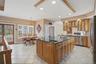 The kitchen features light wood cabinetry, a central island with a dark countertop and integrated sink, stainless steel appliances, and tiled flooring