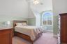 This room features an arched window with a wooded view, a sloped ceiling, and a ceiling fan
