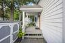 Covered porch with wood decking and white railing, leading to a paneled entry door