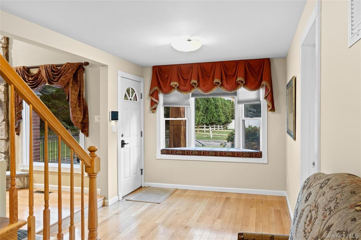 Hardwood-finish flooring, white entry door with decorative glass, window with built-in seating, wood staircase, and stone wall accent