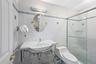 Shower with glass enclosure, white square tile walls with blue accent banding, white pedestal sink with chrome-finish basin, and oval wall mirror