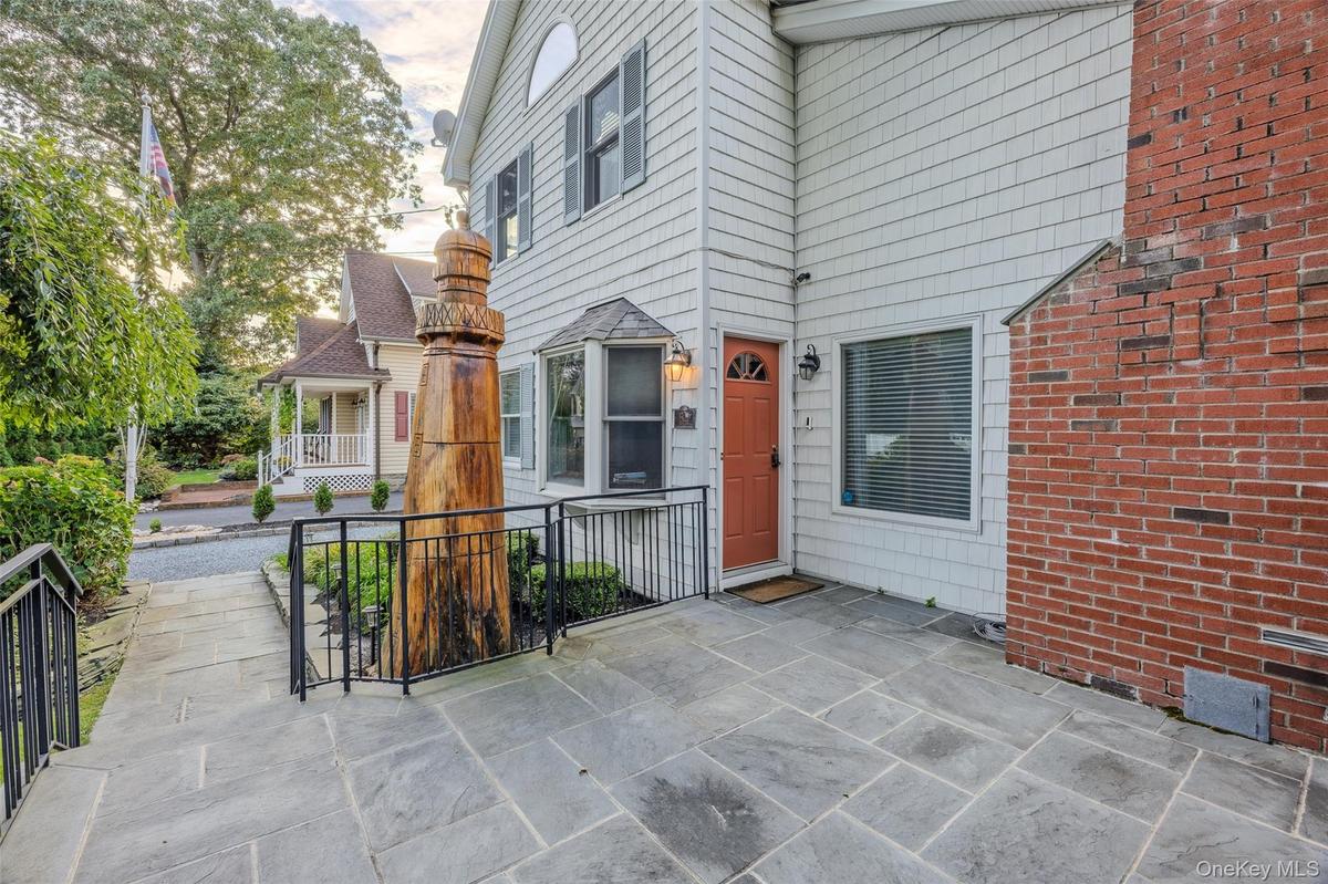 Stone paver patio with black metal railings, white shingle siding, and a prominent brick chimney