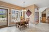The dining area features tiled flooring, a decorative chandelier, and a window offering views of the exterior patio