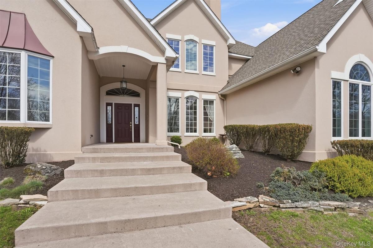 The property features a stucco exterior with a prominent covered entryway, a dark wood front door with sidelights, and arched and bay windows