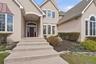 The property features a stucco exterior with a prominent covered entryway, a dark wood front door with sidelights, and arched and bay windows