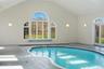 Indoor pool area featuring an arched window, a tiled pool with a blue interior, and access to the outdoors via French doors