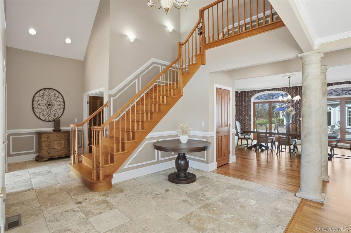 Grand foyer featuring a natural wood staircase with white risers, a vaulted ceiling, and recessed lighting