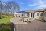 The property features an extensive brick paver patio, a white pergola, and a well-maintained lawn with mature trees