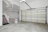 The property features an expansive garage with concrete flooring, a white automatic garage door, and a staircase with carpeted treads and white railin